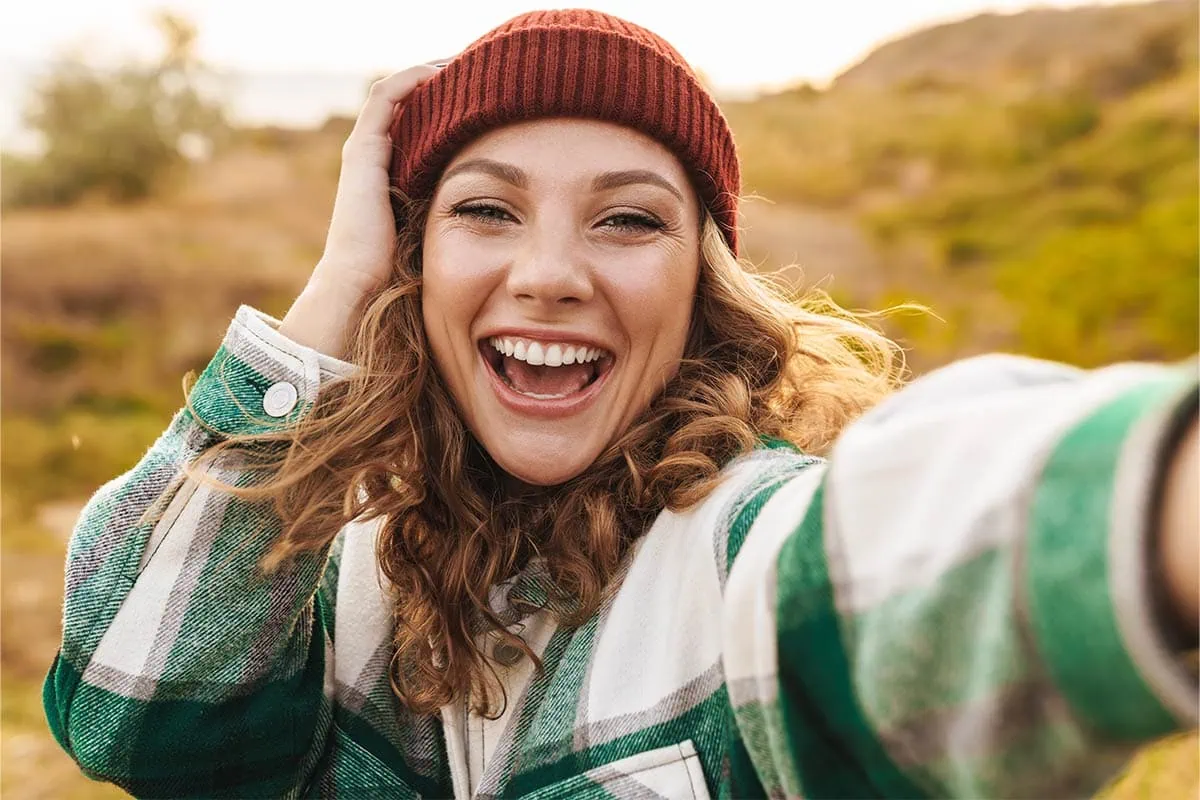 Smiling woman in plaid shirt and red beanie taking an outdoor selfie