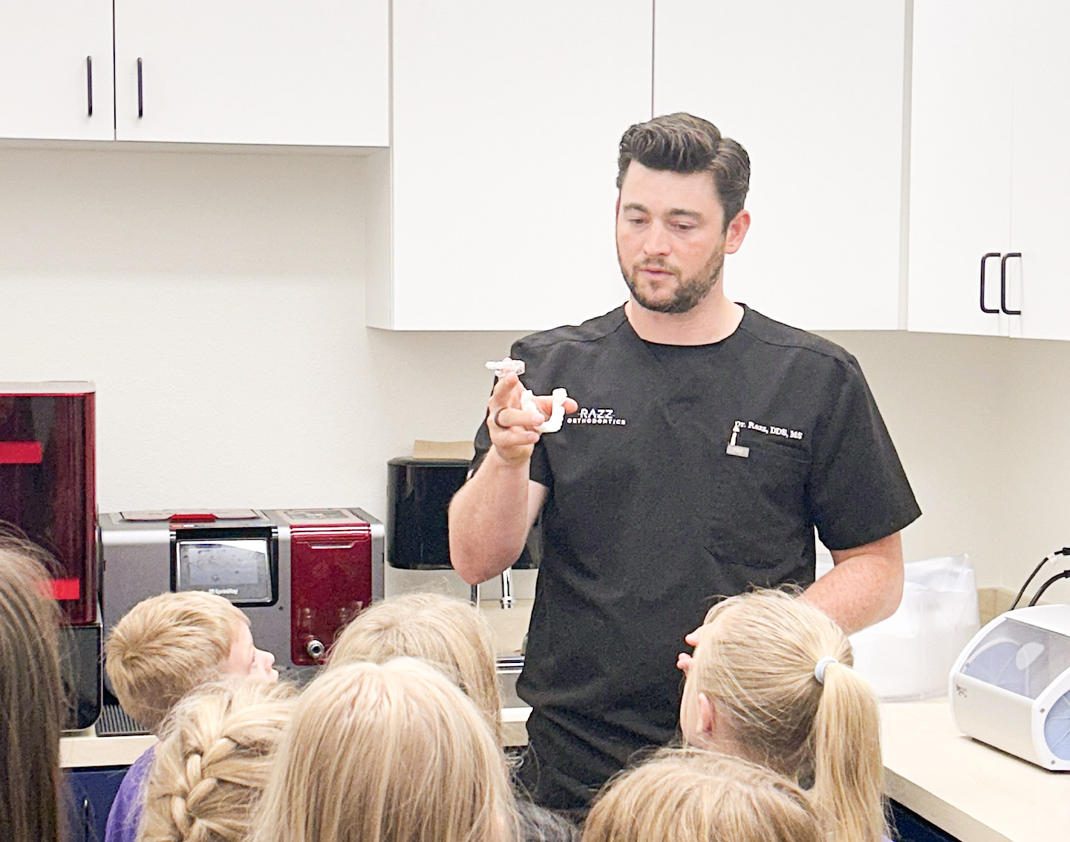 Orthodontist showing clear aligners to children in dental office